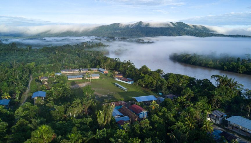 Aerial image of a village near a river with forested mountains in the background.